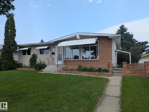 Charming brick ranch home featuring a manicured front lawn, mature landscaping with evergreen plantings, and a welcoming covered entryway - 12835 91 Street Nw, Edmonton, AB - Outdoor