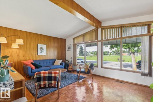 Living area featuring a vaulted ceiling with exposed wood beams, a wood-paneled accent wall, and parquet wood-finish flooring - 12835 91 Street Nw, Edmonton, AB - Indoor Photo Showing Living Room