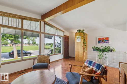 Living area featuring a prominent window wall with clerestory windows, wood-finish flooring, exposed wood beam, a partial-height room divider, and a dark wood entry door - 12835 91 Street Nw, Edmonton, AB - Indoor