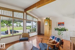 Living area featuring a prominent window wall with clerestory windows, wood-finish flooring, exposed wood beam, a partial-height room divider, and a dark wood entry door - 