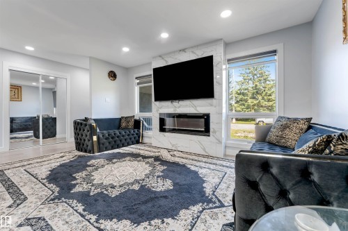 Living area featuring a floor-to-ceiling fireplace with a marble-finish surround and an integrated electric firebox - 7419 33 Avenue Nw, Edmonton, AB - Indoor Photo Showing Living Room With Fireplace