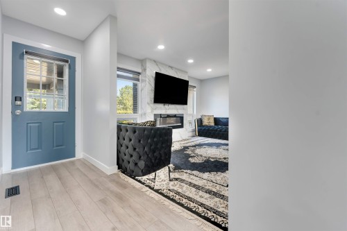 Entryway with light wood-finish flooring and a blue paneled door with glass inserts - 7419 33 Avenue Nw, Edmonton, AB - Indoor Photo Showing Other Room With Fireplace