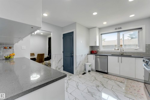 Contemporary kitchen featuring white cabinetry, grey stone countertops, stainless steel appliances, and large format marble-look floor tiles - 7419 33 Avenue Nw, Edmonton, AB - Indoor Photo Showing Kitchen With Upgraded Kitchen