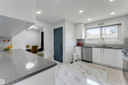 Contemporary kitchen featuring white cabinetry, grey stone countertops, stainless steel appliances, and large format marble-look floor tiles - 