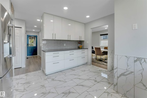 Contemporary kitchen with white high-gloss cabinetry, dark countertops, and a gray subway tile backsplash - 7419 33 Avenue Nw, Edmonton, AB - Indoor Photo Showing Kitchen