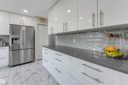 Modern kitchen featuring white high-gloss cabinetry with brushed nickel hardware, a stainless steel French door refrigerator, dark stone countertops, and a textured gray subway tile backsplash - 