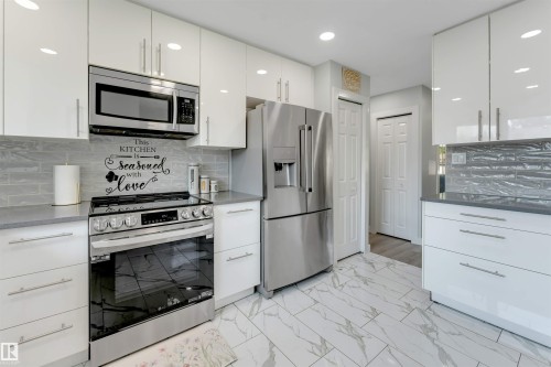 Modern kitchen featuring white cabinetry with silver hardware - 7419 33 Avenue Nw, Edmonton, AB - Indoor Photo Showing Kitchen With Upgraded Kitchen