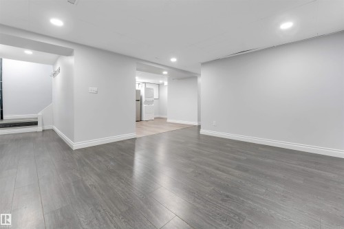 Spacious open-concept room featuring gray wood-finish flooring, recessed lighting, white baseboards, and painted walls - 7419 33 Avenue Nw, Edmonton, AB - Indoor Photo Showing Other Room