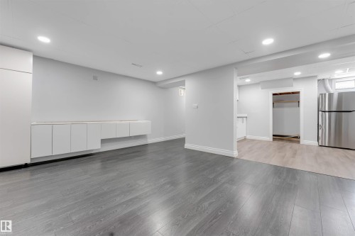 Spacious room with gray wood-finish flooring, white baseboards, recessed lighting, and a long built-in white cabinet unit - 7419 33 Avenue Nw, Edmonton, AB - Indoor