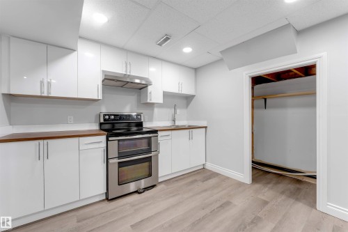 Kitchen featuring white flat-panel cabinetry, wood-finish countertops, and stainless steel appliances including a double oven range and range hood - 7419 33 Avenue Nw, Edmonton, AB - Indoor Photo Showing Kitchen