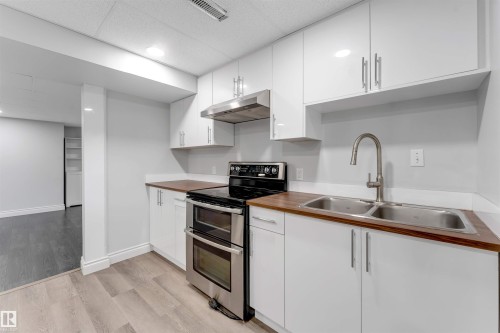 Modern kitchen with white shaker-style cabinetry, wood-finish countertops, stainless steel appliances, and a double basin sink - 7419 33 Avenue Nw, Edmonton, AB - Indoor Photo Showing Kitchen With Double Sink