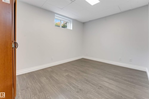 Room featuring light gray walls, wood-finish flooring, white baseboards, a single window, and a drop ceiling with a recessed light fixture - 7419 33 Avenue Nw, Edmonton, AB - Indoor Photo Showing Other Room