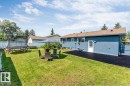 Expansive backyard featuring a manicured lawn, a blue stucco exterior, a brown shingle roof, a paved surface, and a chain-link fence - 7419 33 Avenue Nw, Edmonton, AB  - Outdoor 