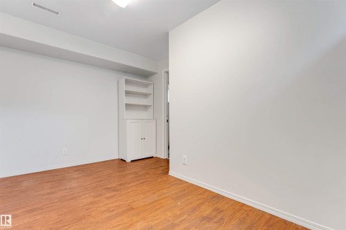 Room featuring wood-finish flooring, white walls, and a built-in white shelving unit with cabinet storage - 7419 33 Avenue Nw, Edmonton, AB - Indoor Photo Showing Other Room