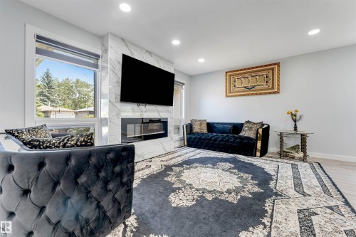 Living area featuring a floor-to-ceiling fireplace with a stone-finish surround, a built-in linear electric firebox, and an integrated display mount - 7419 33 Avenue Nw, Edmonton, AB - Indoor With Fireplace