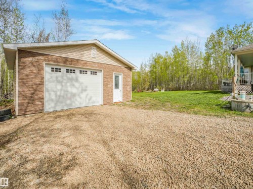 Detached garage featuring a paneled overhead door with rectangular window inserts, a side entry door with frosted glass, and a gravel driveway - 16 Crystal Keys Crescent, Rural Wetaskiwin County, AB - Outdoor