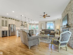 Open concept living area featuring wood-finish flooring, a stone accent wall with fireplace, and a kitchen with stainless steel appliances and a multi-light pendant island - 