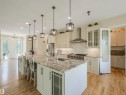 Expansive kitchen featuring a large island with seating, pendant lighting, stone countertops, stainless steel appliances, and wood-finish flooring - 16 Crystal Keys Crescent, Rural Wetaskiwin County, AB  - Indoor Photo Showing Kitchen With Upgraded Kitchen 