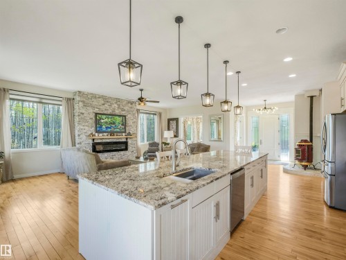Open-concept living space featuring wood-finish flooring, a stone-clad fireplace, and a kitchen island with stone countertops - 16 Crystal Keys Crescent, Rural Wetaskiwin County, AB - Indoor Photo Showing Kitchen With Double Sink With Upgraded Kitchen