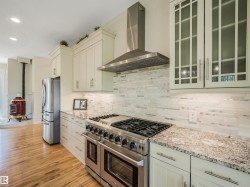 Gourmet kitchen featuring a professional-grade gas range with a stainless steel range hood, stone countertops, and a full-height tile backsplash - 