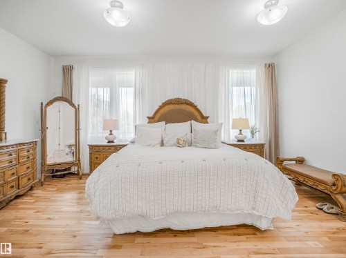 Bright room featuring light wood-finish flooring, white walls, and two windows with sheer and opaque curtains - 16 Crystal Keys Crescent, Rural Wetaskiwin County, AB - Indoor Photo Showing Bedroom