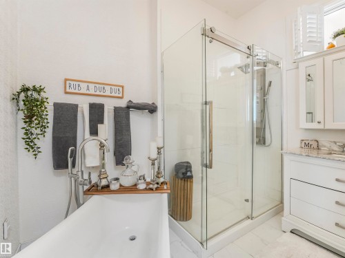 Spacious bathroom featuring a frameless glass shower enclosure, a freestanding soaking tub with a floor-mounted faucet, a vanity with a stone countertop, and white plantation shutters - 16 Crystal Keys Crescent, Rural Wetaskiwin County, AB - Indoor Photo Showing Bathroom