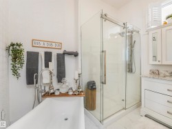 Spacious bathroom featuring a frameless glass shower enclosure, a freestanding soaking tub with a floor-mounted faucet, a vanity with a stone countertop, and white plantation shutters - 