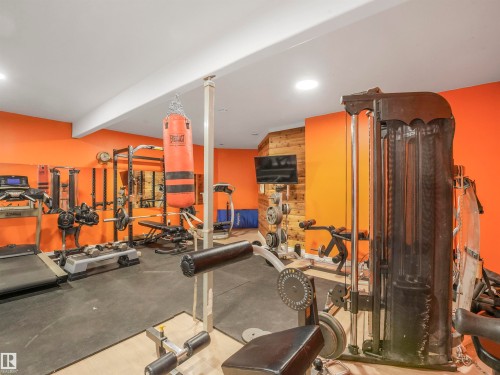 Dedicated fitness space featuring rubberized flooring, vibrant orange accent walls, recessed lighting, and a wood-paneled feature wall - 16 Crystal Keys Crescent, Rural Wetaskiwin County, AB - Indoor Photo Showing Gym Room