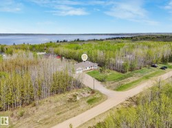Expansive property featuring a single-story home, a private gravel road, mature trees, and proximity to a large body of water - 
