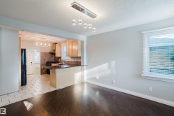 Open-concept living area featuring dark wood-finish flooring, a contemporary linear chandelier, and a bright window with blinds - 