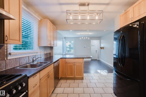 Kitchen featuring light wood cabinetry, dark countertops, a stainless steel double sink, a black range, and a black refrigerator - 12431 81 Street Nw, Edmonton, AB - Indoor Photo Showing Kitchen With Double Sink