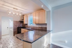 Kitchen featuring a peninsula with a dark countertop, light wood-finish cabinetry, a stainless steel range hood, and a tiled backsplash - 