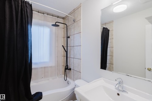 Bathroom featuring a white bathtub, a matte black rainfall shower head with handheld attachment, full tile surround, a built-in window, and a vanity with a white ceramic sink - 12431 81 Street Nw, Edmonton, AB - Indoor Photo Showing Bathroom