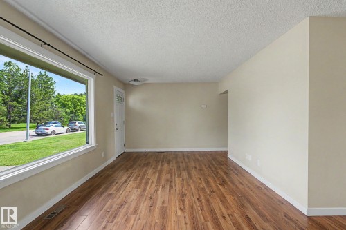 Spacious room featuring wood-finish flooring, light-toned walls, and a large picture window - 8823 130A Avenue Nw, Edmonton, AB - Indoor Photo Showing Other Room