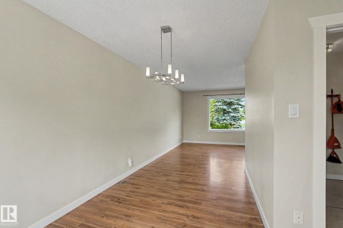 Spacious interior with wood-finish flooring, a modern chandelier, and a large window overlooking mature greenery - 8823 130A Avenue Nw, Edmonton, AB - Indoor Photo Showing Other Room