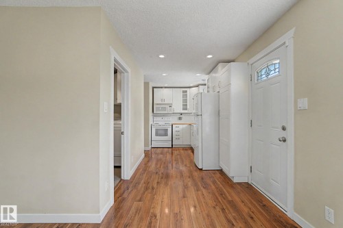 Wood-finish flooring throughout, with a white entry door featuring decorative glass - 8823 130A Avenue Nw, Edmonton, AB - Indoor Photo Showing Other Room