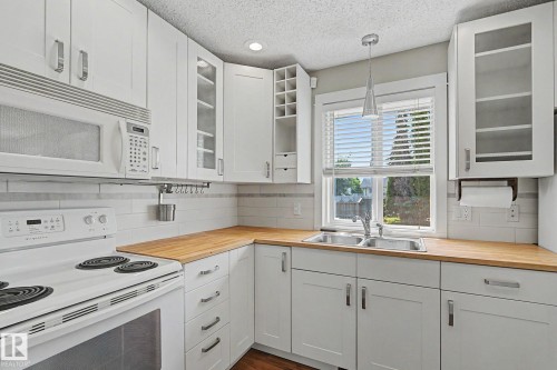 White cabinetry with brushed nickel hardware, wood-finish countertops, subway tile backsplash, stainless steel double basin sink, and a built-in microwave - 8823 130A Avenue Nw, Edmonton, AB - Indoor Photo Showing Kitchen With Double Sink