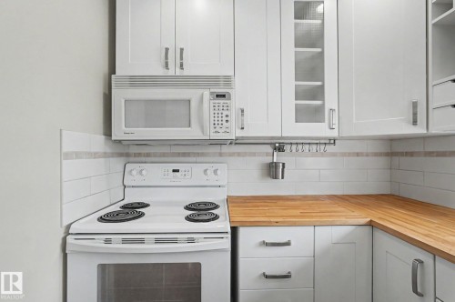 Kitchen featuring white cabinetry, wood-finish countertops, white subway tile backsplash, and a white electric range with an overhead microwave - 8823 130A Avenue Nw, Edmonton, AB - Indoor Photo Showing Kitchen