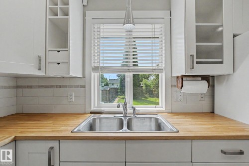 Kitchen featuring a double stainless steel sink, wood-finish countertops, white shaker cabinetry, subway tile backsplash, and a window with blinds - 8823 130A Avenue Nw, Edmonton, AB - Indoor Photo Showing Kitchen With Double Sink