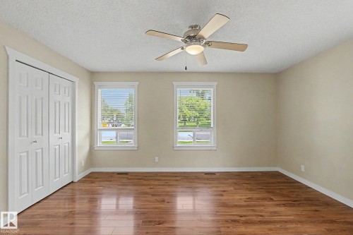 Spacious room featuring wood-finish flooring, two windows with white blinds, a ceiling fan with integrated lighting, and a bi-fold closet with panel doors - 8823 130A Avenue Nw, Edmonton, AB - Indoor Photo Showing Other Room