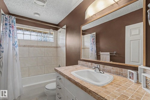 Bathroom featuring a white vanity with a tiled countertop, a built-in sink, and a large mirror - 8823 130A Avenue Nw, Edmonton, AB - Indoor Photo Showing Bathroom