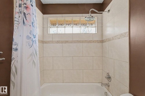 Bathtub and shower combination featuring neutral-toned wall tiles, a decorative mosaic tile accent, a glass block window, and a chrome rainfall showerhead - 8823 130A Avenue Nw, Edmonton, AB - Indoor Photo Showing Bathroom