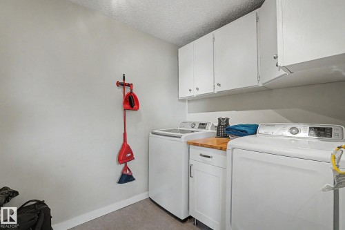 Dedicated laundry space featuring white upper cabinetry, a wood-finish countertop, and base cabinetry with a drawer - 8823 130A Avenue Nw, Edmonton, AB - Indoor Photo Showing Laundry Room