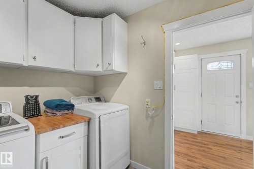 Dedicated laundry space featuring white cabinetry, a wood-finish countertop, and ample overhead storage - 8823 130A Avenue Nw, Edmonton, AB - Indoor Photo Showing Laundry Room