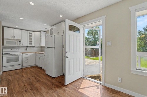 Kitchen featuring wood-finish flooring, white cabinetry, a white tile backsplash, and light wood countertops - 8823 130A Avenue Nw, Edmonton, AB - Indoor Photo Showing Kitchen
