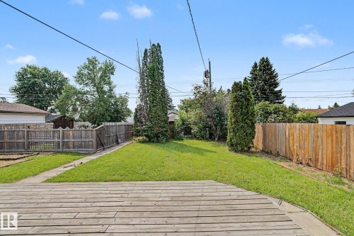 Expansive backyard featuring a wood deck, a manicured lawn, and mature trees, enclosed by wood fencing - 8823 130A Avenue Nw, Edmonton, AB - Outdoor