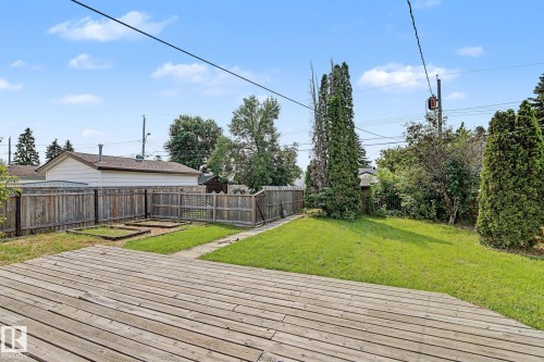 Expansive backyard featuring a spacious wood deck, manicured lawn, raised garden beds, and mature perimeter trees - 8823 130A Avenue Nw, Edmonton, AB - Outdoor