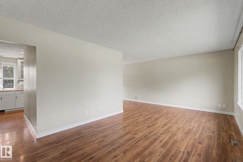 Spacious living area featuring wood-finish flooring, light-toned wall paint, and white trim - 8823 130A Avenue Nw, Edmonton, AB - Indoor Photo Showing Other Room