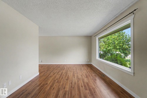Spacious room featuring wood-finish flooring and a large picture window - 8823 130A Avenue Nw, Edmonton, AB - Indoor Photo Showing Other Room
