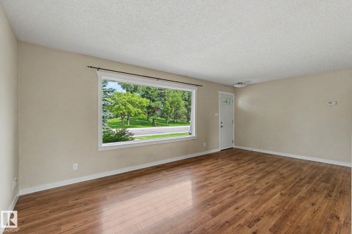 Bright interior space featuring a large picture window, wood-finish flooring, light neutral wall paint, white trim, and a white entry door with decorative glass - 8823 130A Avenue Nw, Edmonton, AB - Indoor Photo Showing Other Room